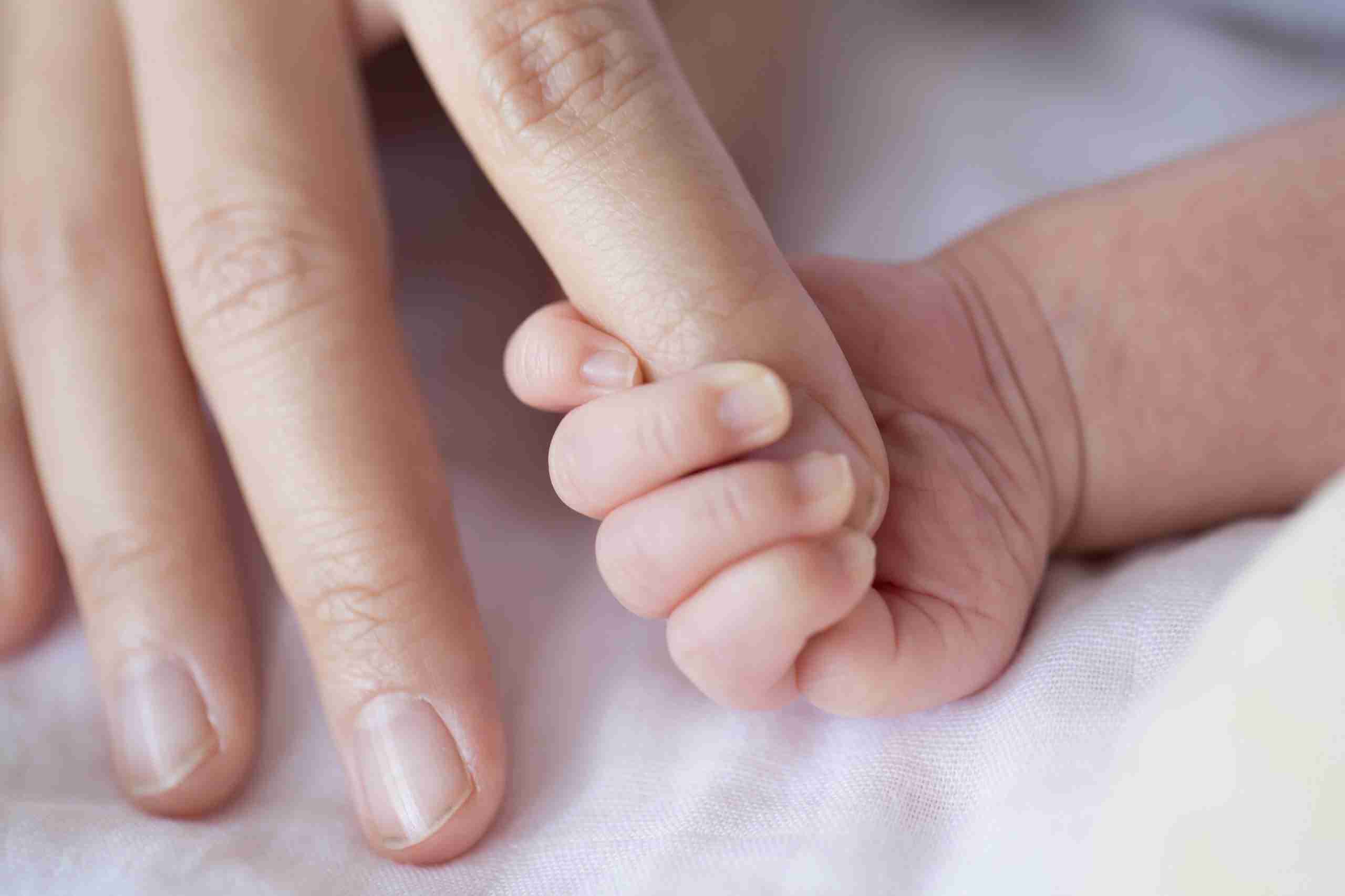 closeup of infant holding an adult's finger