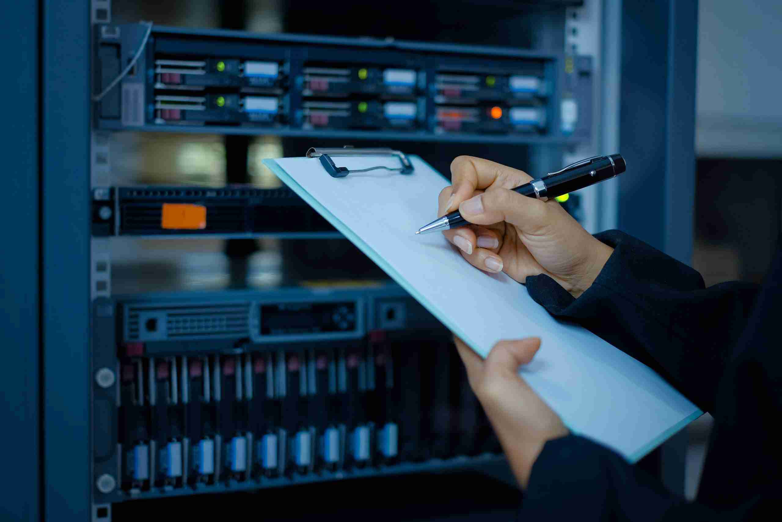 new year security checklist - someone writing on a clipboard in front of tech equipment