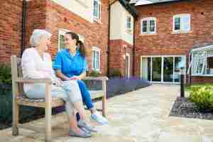 senior woman sitting outside on a bench talking to a nurse
